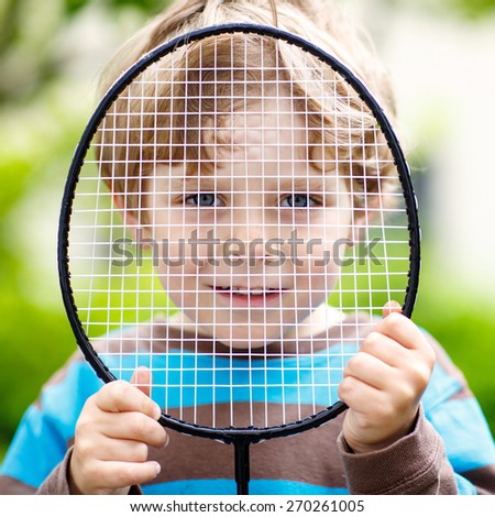 Little cute funny kid boy with badminton racquet playing in domestic garden. Active outdoors games and leisure for children lifestyle.