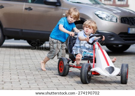 Two happy children having fun with toy race car in summer garden, outdoors. Active brother pushing the car with younger boy. Outdoor games for children in summer concept.