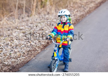 Happy little cyclist boy riding bike and having fun on cold  day, outdoors. Active leisure with children in winter, sping or autumn.