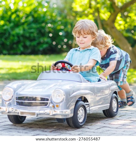 Two funny little friends playing with big old toy car in summer garden, outdoors. Active leisure with kids on warm summer day.