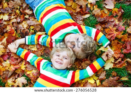 Two little kid boys lying in autumn leaves in colorful clothing. Happy siblings having fun in autumn park on warm day.