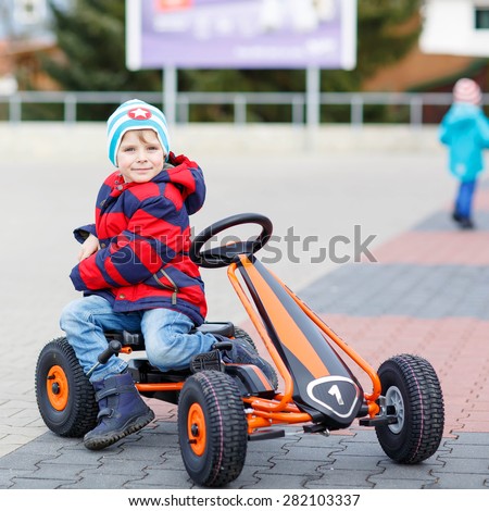 Funny little kid boy having fun with toy race cars, outdoors. Child driving car. Outdoor games for children concept.