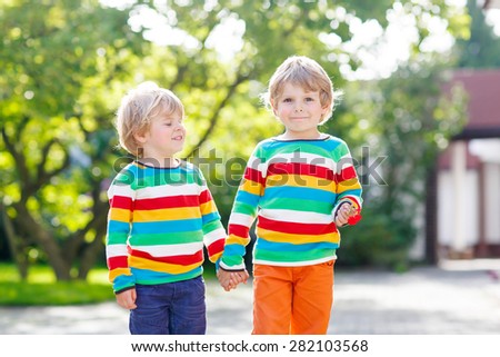 Two little siblings in colorful clothing walking hand in hand and hugging in summer or autumn garden. Brother love