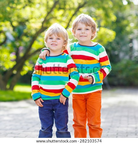 Two little friends boys friends in colorful clothing walking hand in hand and hugging in summer or autumn garden.  Friendship concept.