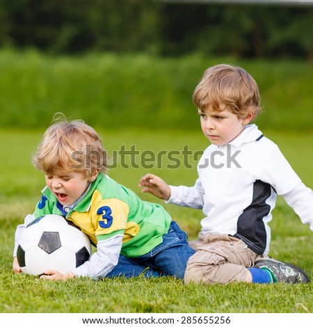 Two active twins playing soccer and football and having fun on field, outdoors. Active leisure with children on warm sunny summer day.