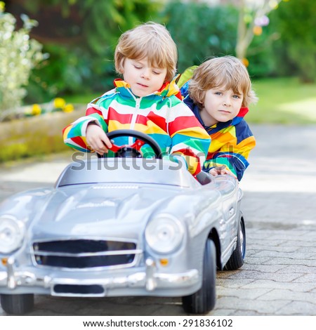 Two funny sibling kid boys playing with big old vintage toy car in spring or autumn garden, outdoors. Active leisure with kids outdoors  on warm spring or autumn day.