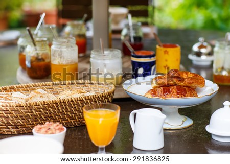 Table laid for breakfast outside in summer with various jams, bread, coffee, croissants, muesli and orange juice. French breakfast. Provence, France