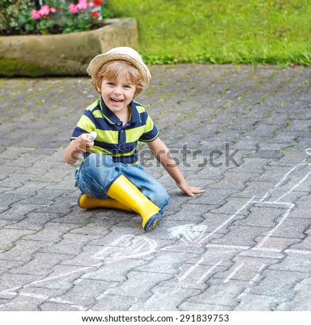 Cute little child drawing a picture of a vehicle with chalk in summer. Creative leisure for kids in summer. Boy in yellow rubber boots.
