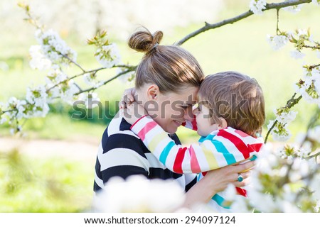 Young woman and her little son, blond kid boy in blooming cherry garden in spring. Happy family enjoying nature, togetherness and celebrating mother\'s day.