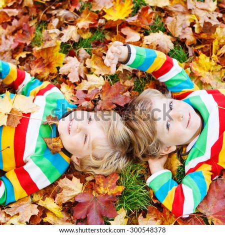 Two blond boys lying in autumn leaves in colorful clothing. Happy siblings having fun in autumn park on warm day.
