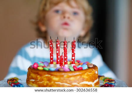 Funny blond kid celebrating his birthday and blowing candles on homemade baked cake, indoor. Birthday party for kids. Focus on cake