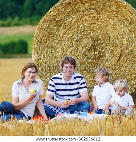 Mother, father and two little children, kid boys having picnic on yellow hay field in summer, outdoors. Family having fun together.