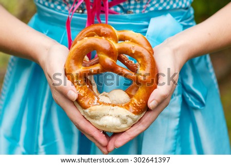 Oktoberfest pretzels in hands of a woman in traditional German clothes, blue bavarian dirndl. Bread as traditional food on festival in Germany.