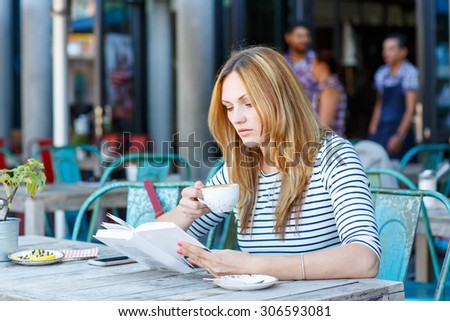 Young beautiful girl drinking coffee and reading book in an outdoor cafe in London, United Kingdom