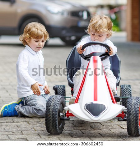 Funny kid boys, best friends, playing with toy car in summer garden, outdoors. Children having fun in domestic garden or nursery on sunny warm day.