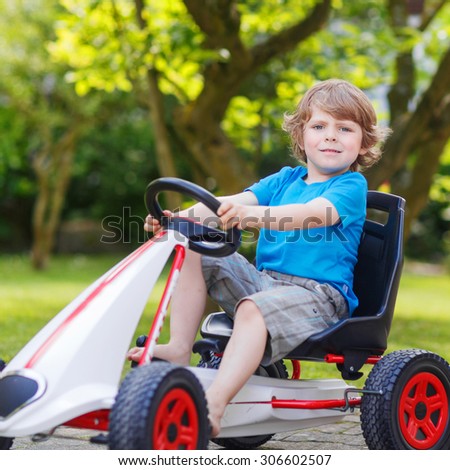 Funny happy  little kid boy having fun and driving toy race car in home's garden. Active games for children in summer. On warm sunny day.