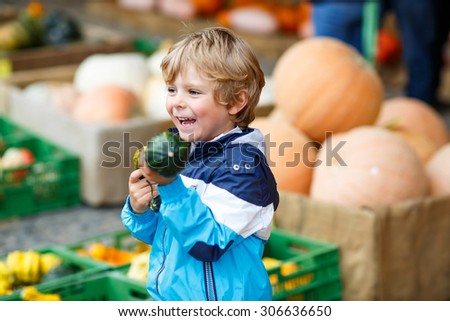 Happy blond kid boy holding green pumpkin on halloween or thanksgiving harvest festival or patch, outdoors