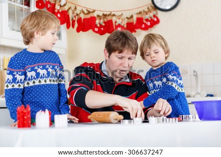 Two funny boys, sons and father baking gingerbread cookies. Happy siblings, children in blue xmas pullovers. Kitchen decorated for Christmas. Family, holiday, kids lifestyle concept.