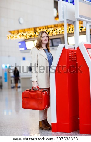 Business woman at international airport, checking in on electronic terminal waiting for her flight. Female passenger at terminal, indoors. Airport decorated for Christmas
