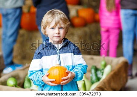 Adorable blond kid boy holding orange pumpkin on halloween or thanksgiving harvest festival or patch, outdoors