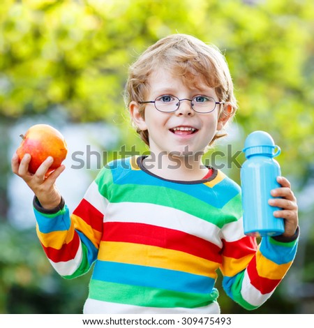Funny little boy with apple and drink bottle on his first day to elementary school or nursery. Outdoors.  Back to school, kids, lifestyle concept