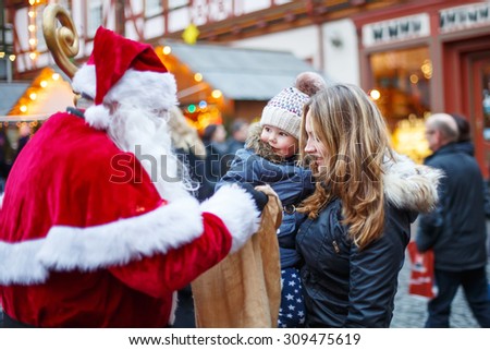 Little toddler girl with mother on Christmas market. Funny happy kid taking gift from bag of Santa Claus. holidays, christmas, childhood and people concept