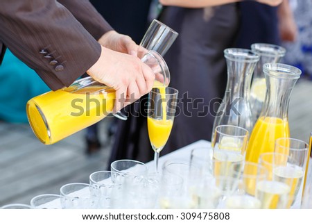 Hand of a man pouring orange juice on a wedding in summer