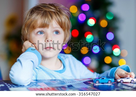Adorable child playing with cars and toys at home, indoor. funny boy having fun with gifts. Colorful christmas lights on background. Family, holiday, kids lifestyle concept.