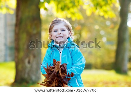 Funny blond child with a lot of yellow autumn leaves in park. Kid boy having fun on sunny warm october day. Season, children, lifestyle concept