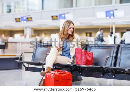 Business woman at international airport sitting and drinking coffee to go while waiting for her flight for a business trip. Female passenger at terminal, indoors.  Travel, business, people concept.