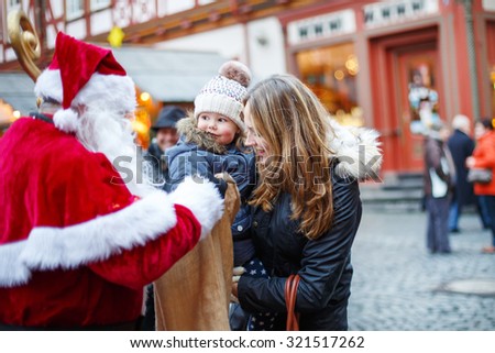 Little toddler girl with mother on Christmas market. Funny happy kid taking gift from bag of Santa Claus. holidays, christmas, childhood and people concept