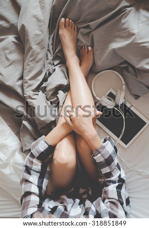 Soft photo of woman in checkered shirt on the bed with tablet and headphones, top view point