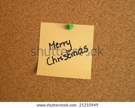 Yellow small sticky note on an office cork bulletin board. Merry Christmas.