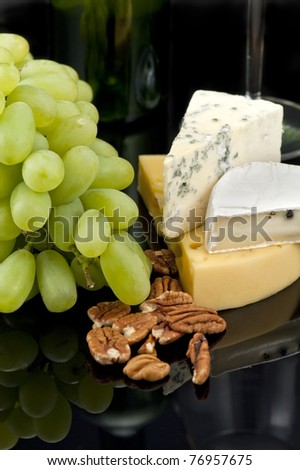 Grapes, nuts and cheese on black reflected background