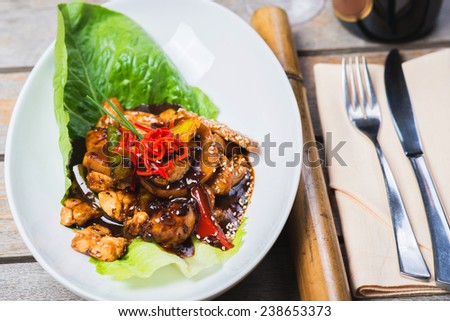 pieces of chicken cooked in black bean sauce on a wooden table in a restaurant with white wine and decorated with an Asian background
