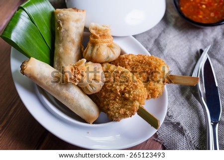 Asian Starters - wontons, chicken satay and spring rolls served with sweet chili sauce and lemonade on the wooden table
