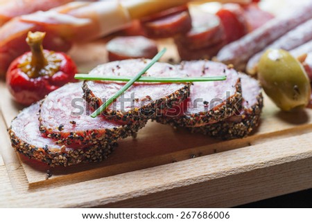close up of mix of traditional spanish ham salami parma ham on grissini bread sticks, marinated vegetables and olives on wooden plate with rustic decor
