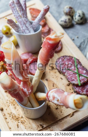 mix of traditional spanish ham salami parma ham on grissini bread sticks, marinated vegetables and olives on wooden plate with rustic decor