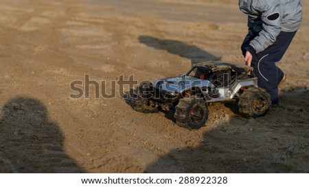 child with a radio-controlled model monster truck on the sandy ground in the park. soft focus and beautiful bokeh