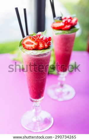 two glasses of cold bright juicy and delicious berry smoothie of strawberries and currants with the decor of fresh berries on a summer day on a table in a restaurant. soft focus and beautiful bokeh.