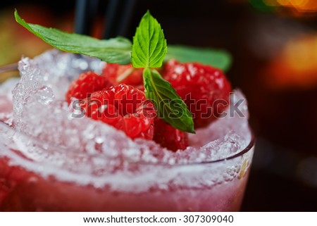 bright beautiful and tasty alcoholic cocktail or lemonade with a cap of frozen ice and fresh raspberries on the bar with a nice bokeh of the disco light. soft focus.