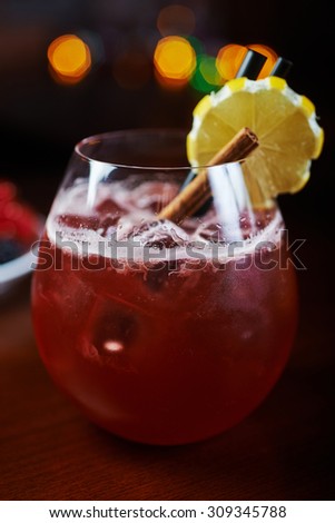 glass of delicious alcoholic cocktails or lemonade with ice, decoration of fresh berries and a slice of lemon on a wooden table in a bar or restaurant with a beautiful bokeh in the background