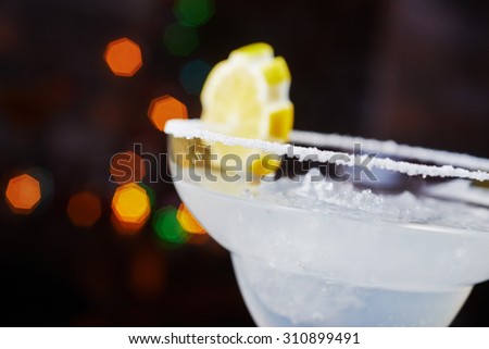 bright refreshing cocktail daiquiri on a table in a restaurant with creative decoration of orange slices and ice in a bar with a beautiful disco lights bokeh in the background. soft focus.