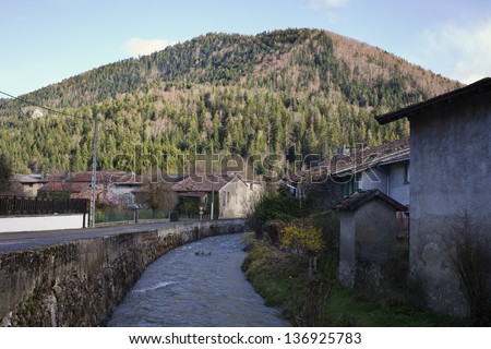 Near the Pirinei\'s mountains a river cross a small village in a sunny day