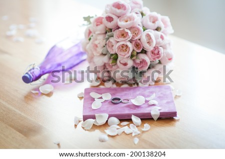 Wedding bouquet of beautiful david austen roses lying on the table next to a purple notebook and wedding rings