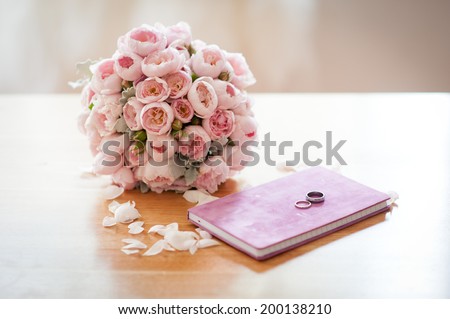 Wedding bouquet of beautiful david austen roses lying on the table next to a purple notebook and wedding rings