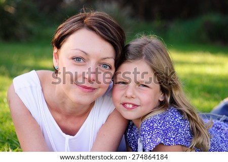 A close up portrait of a young beautiful mum and her adorable daughter outdoors in a park on a sunny summer day