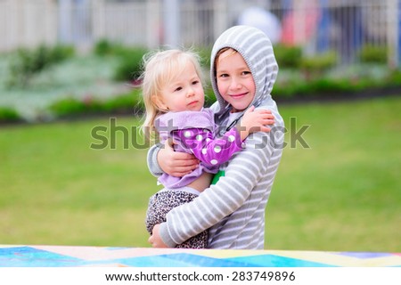 A portrait of a happy big brother holding his little toddler sister in a park on a cool summer or autumn day