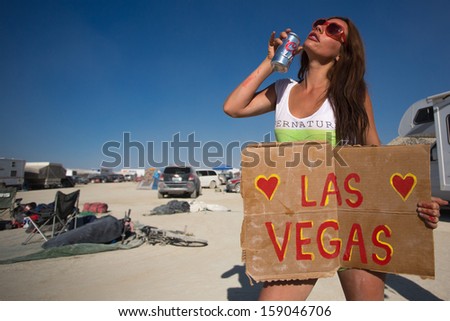 BLACK ROCK DESERT, NEVADA, SEPTEMBER 3: Unidentified sexy woman holding a sign, looking for a ride back to Las Vegas while drinking a beer after a musical festival in the USA. September 3, 2013.