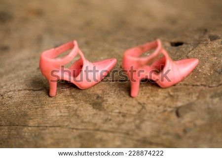 Defocussed pink toy women shoes made of plastic or high heels on wood background.